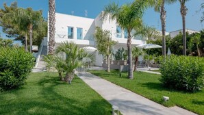 A modern building with a white facade, surrounded by well-maintained greenery and palm trees. - Suite Fontanelle Luxury 8 by Salentoaffitti (Torre San Giovanni)