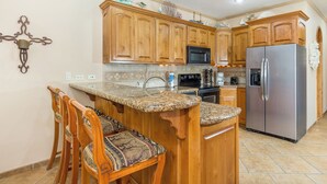 Una cocina con armarios de madera, encimeras de granito, un refrigerador de acero inoxidable y una zona de bar con dos sillas.