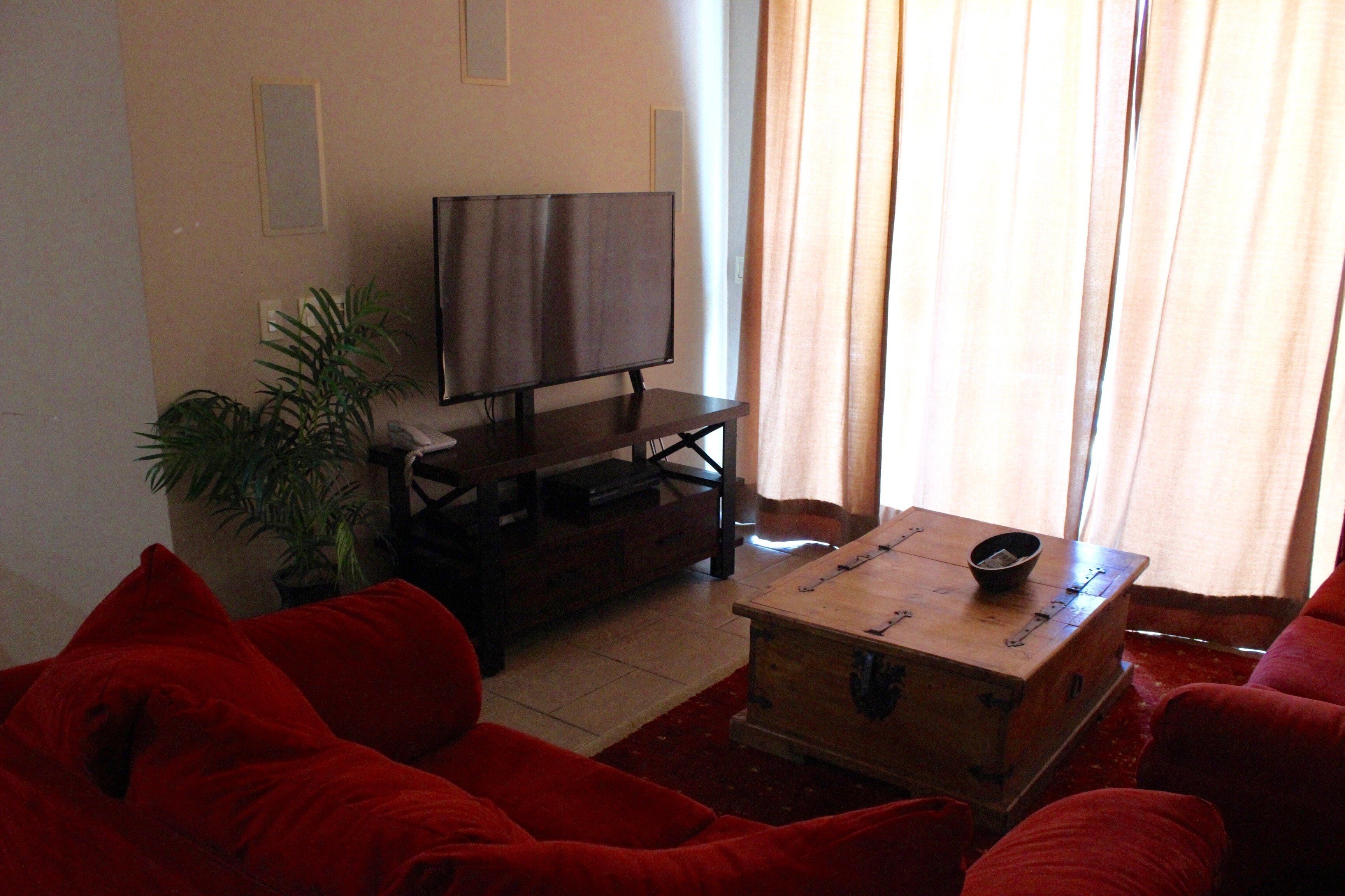 A living room with a flat-screen TV on a stand, a wooden coffee table, and red sofas.