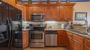A kitchen with wooden cabinets, stainless steel appliances, a granite countertop, and a tiled backsplash. - Casa Blanca (Puerto Peñasco)