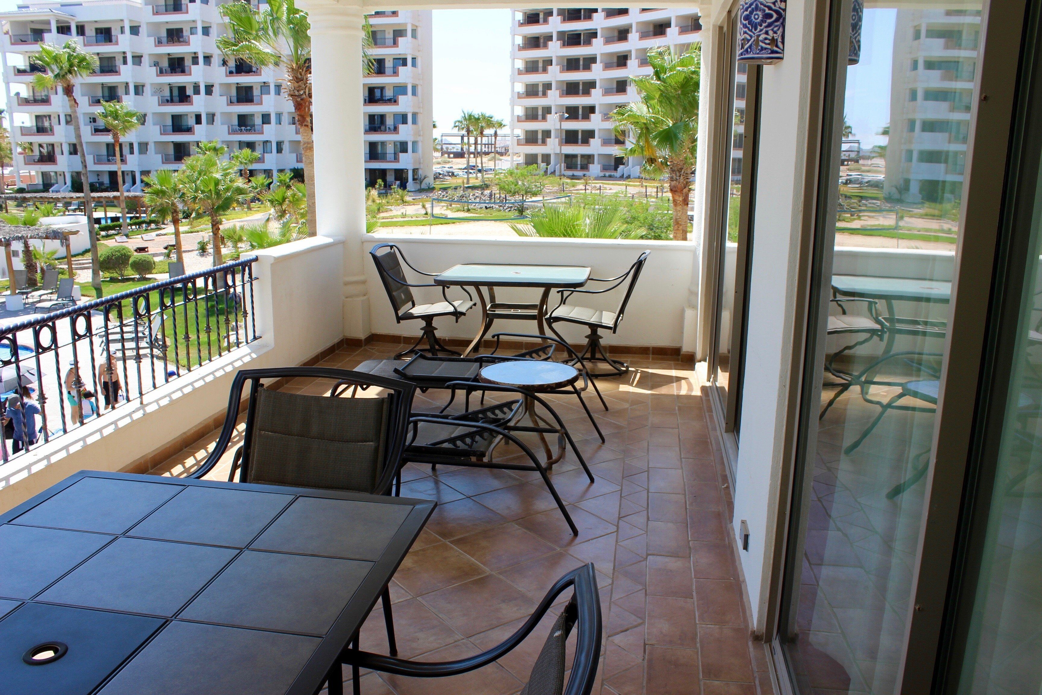 Ein Balkon mit Tisch und Stühlen, der auf ein Wohngebiet mit Palmen und Mehrfamilienhäusern blickt.