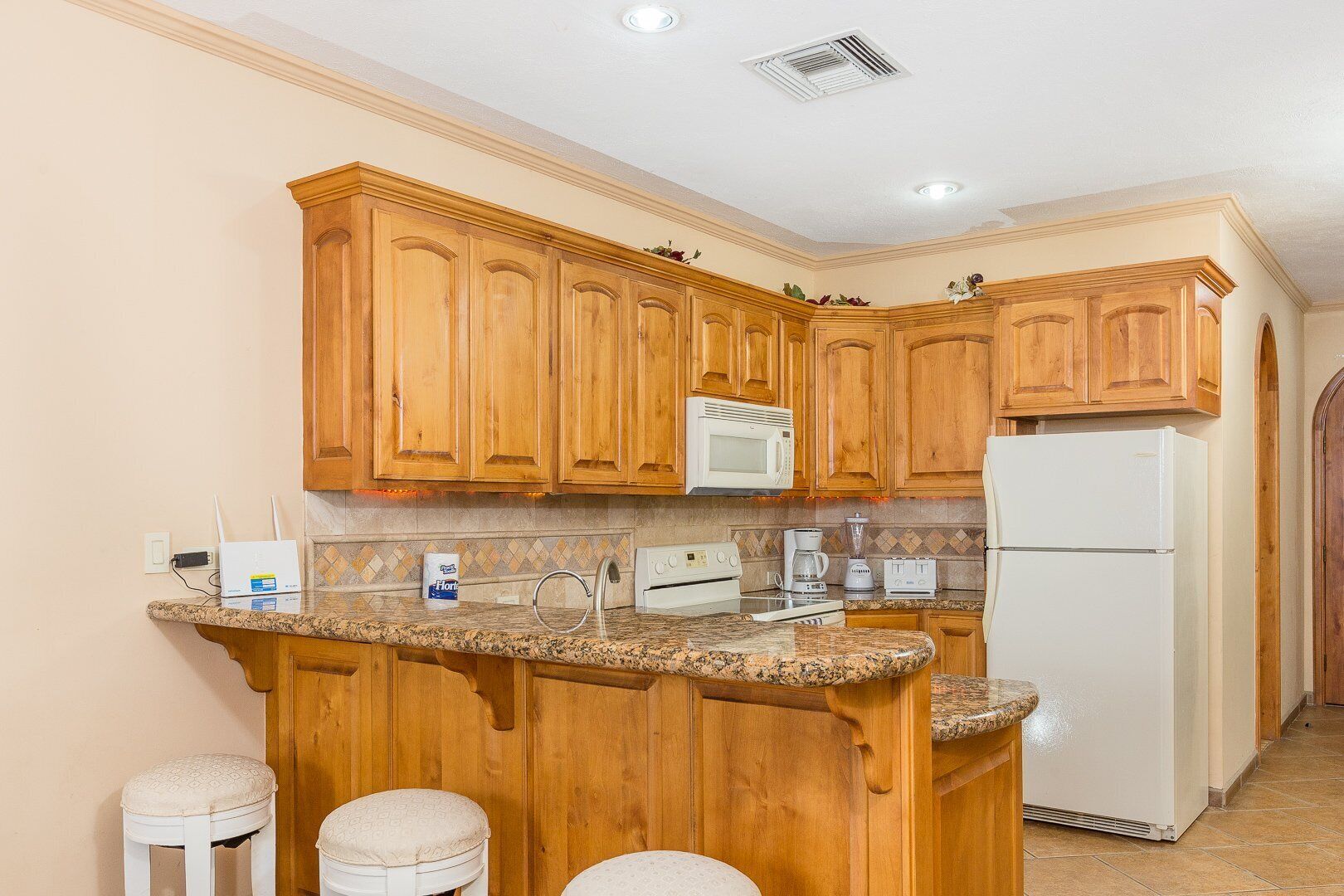 Una cocina con armarios de madera, encimera de granito, microondas, cafetera y refrigerador.