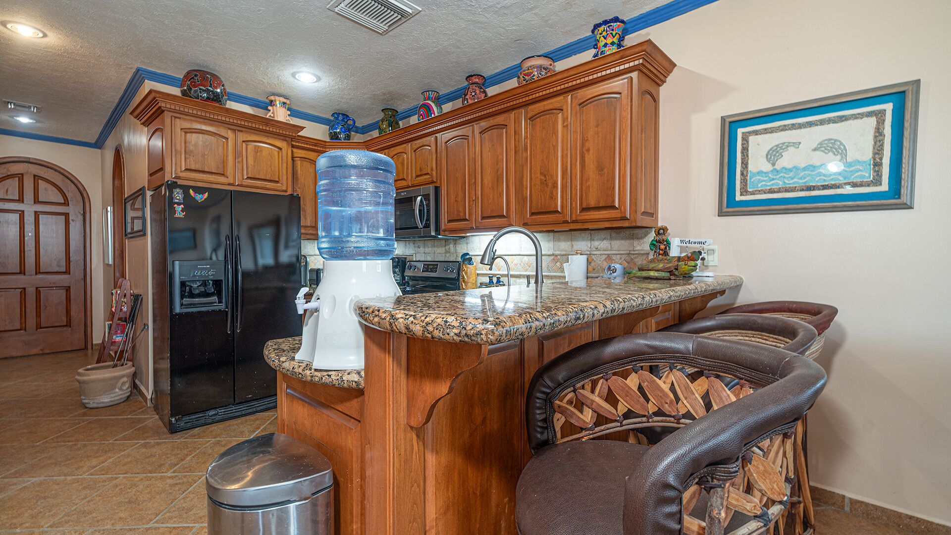 A kitchen with wooden cabinets, a water dispenser, a refrigerator, and a sink.