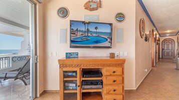 Ein Wohnzimmer mit Fernseher, der eine Strandansicht zeigt, einer Holzunterhaltungsecke mit elektronischen Geräten und einem Schild mit der Aufschrift 'THE OCEAN FIXES EVERYTHING'.