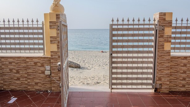 Uitzicht op het strand door een hek met een decoratief beeld en een stenen muur.