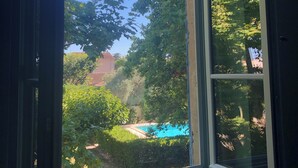 Une vue à travers une fenêtre, avec un ciel bleu dégagé, une piscine et une végétation luxuriante tout autour.