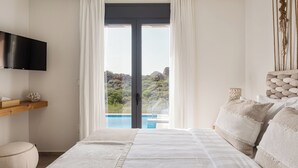 Ein Schlafzimmer mit Bett, einem an der Wand montierten Fernseher, einem Fenster mit Vorhängen und Blick auf Pool und Gartenlandschaft.