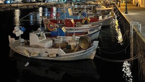 Ein Hafen bei Nacht mit vertäuten Booten, ein markanter Felsen im Hintergrund und Gebäude mit beleuchteten Schildern.