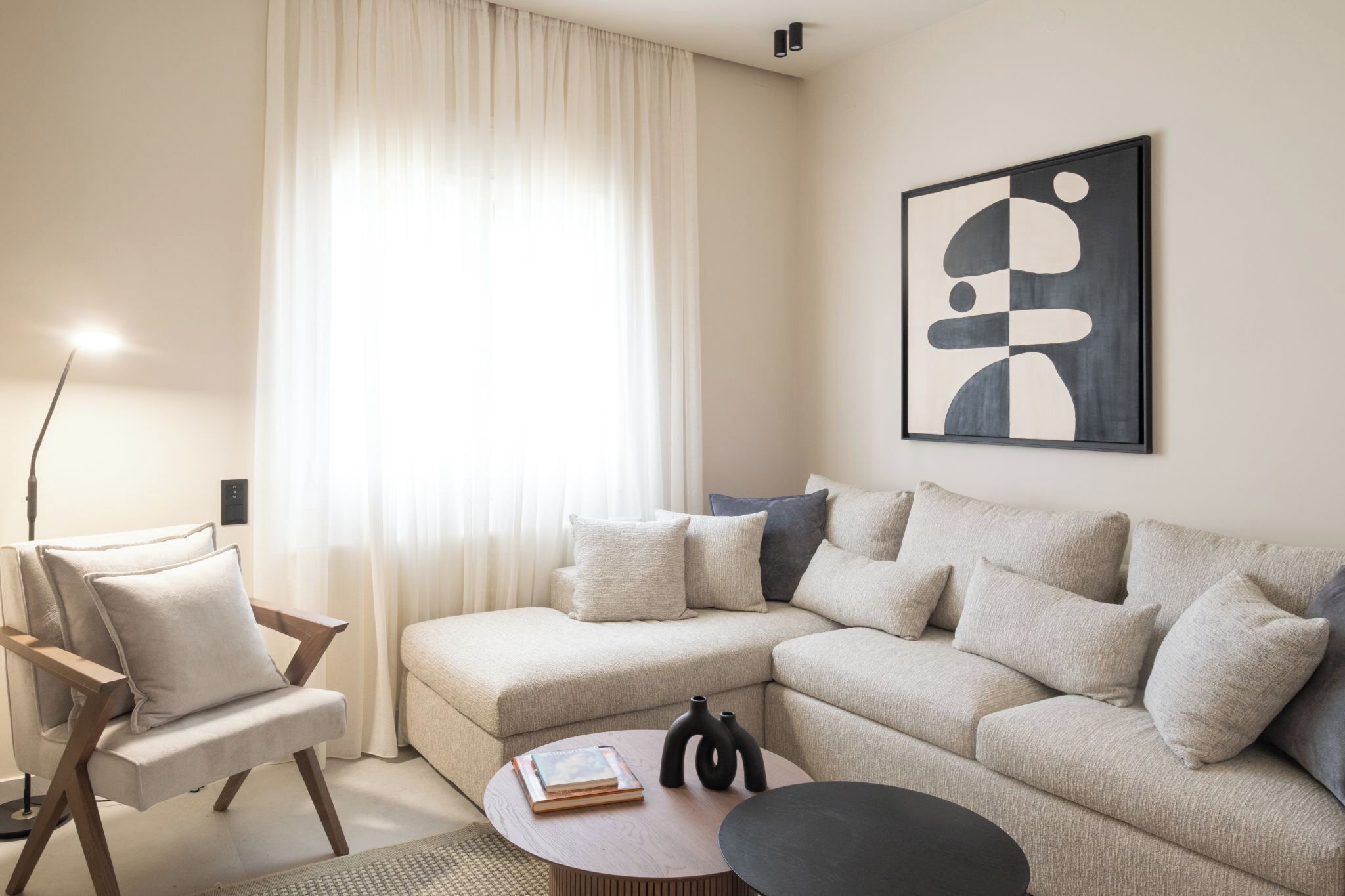 A modern living room with a beige sectional sofa, a wooden chair, a round coffee table, and a large abstract painting on the wall.