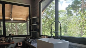 A modern kitchen with a large window, a sink, and wooden shelves. - Escape to Luxury in the Cangrejal River Valley – A Jungle Retreat Awaits! (Atlántida Department)