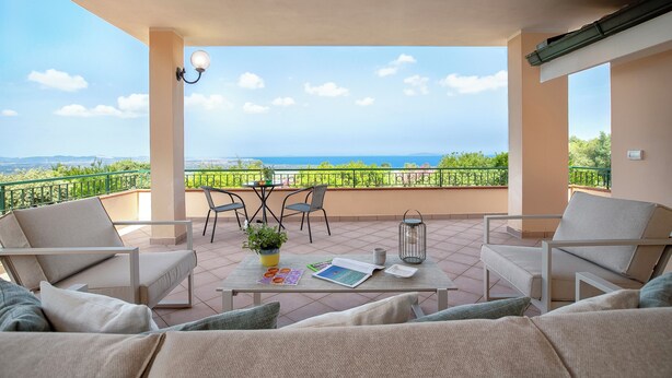 A balcony with a view of the sea, furnished with two chairs and a table, and a potted plant.