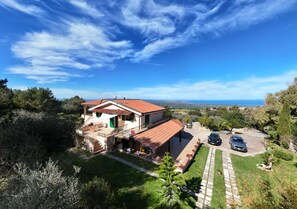 A two-story house with a red-tiled roof, a covered patio, and a driveway with two cars parked.