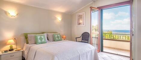 A bedroom with a bed, bedside lamps, a chair, and a balcony with a view.