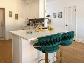 Una cocina con una isla blanca, taburetes de bar y una puerta al fondo.