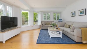 En rummelig stue med et stort fladskærms-tv, en beige sofa, et sofabord og en blå pude med et mønster.