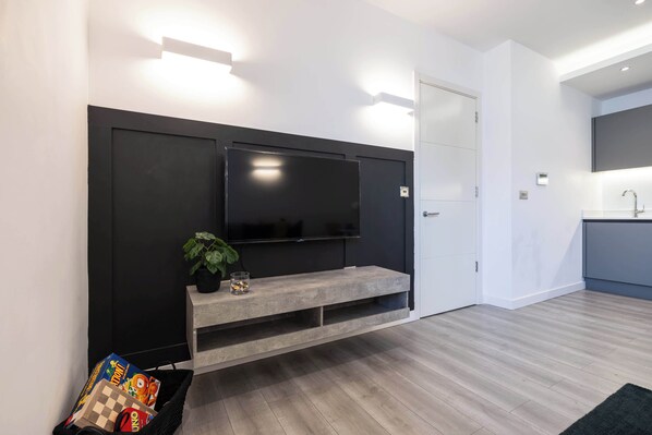 Una sala de estar moderna con un televisor de pantalla plana montado en una pared negra, un mueble de madera debajo y una planta pequeña sobre el mueble.