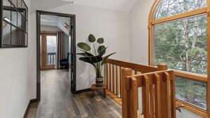 A modern interior with a wooden staircase, a large window with a forest view, and a potted plant.