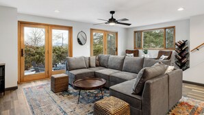 A modern living room with a sectional sofa, a coffee table, and a large window with a view of trees.