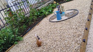 Ein Gartenbereich mit Kiesgrund, Holzumrandung und einem kleinen Brunnen.