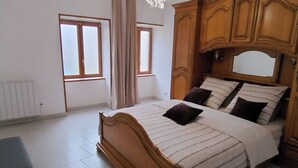 Ein Schlafzimmer mit einem Holzbett, zwei mit Vorhängen versehenen Fenstern, einem Heizkörper und einer Chandelier.