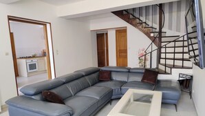 Ein Wohnzimmer mit einer Eckcouch, einem Glastisch und einer Treppe mit Metallgeländer.