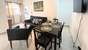 En moderne stue med en sort sofa, et spisebord med sorte stole, en ventilator i loftet og et fladskærms-TV monteret på væggen.