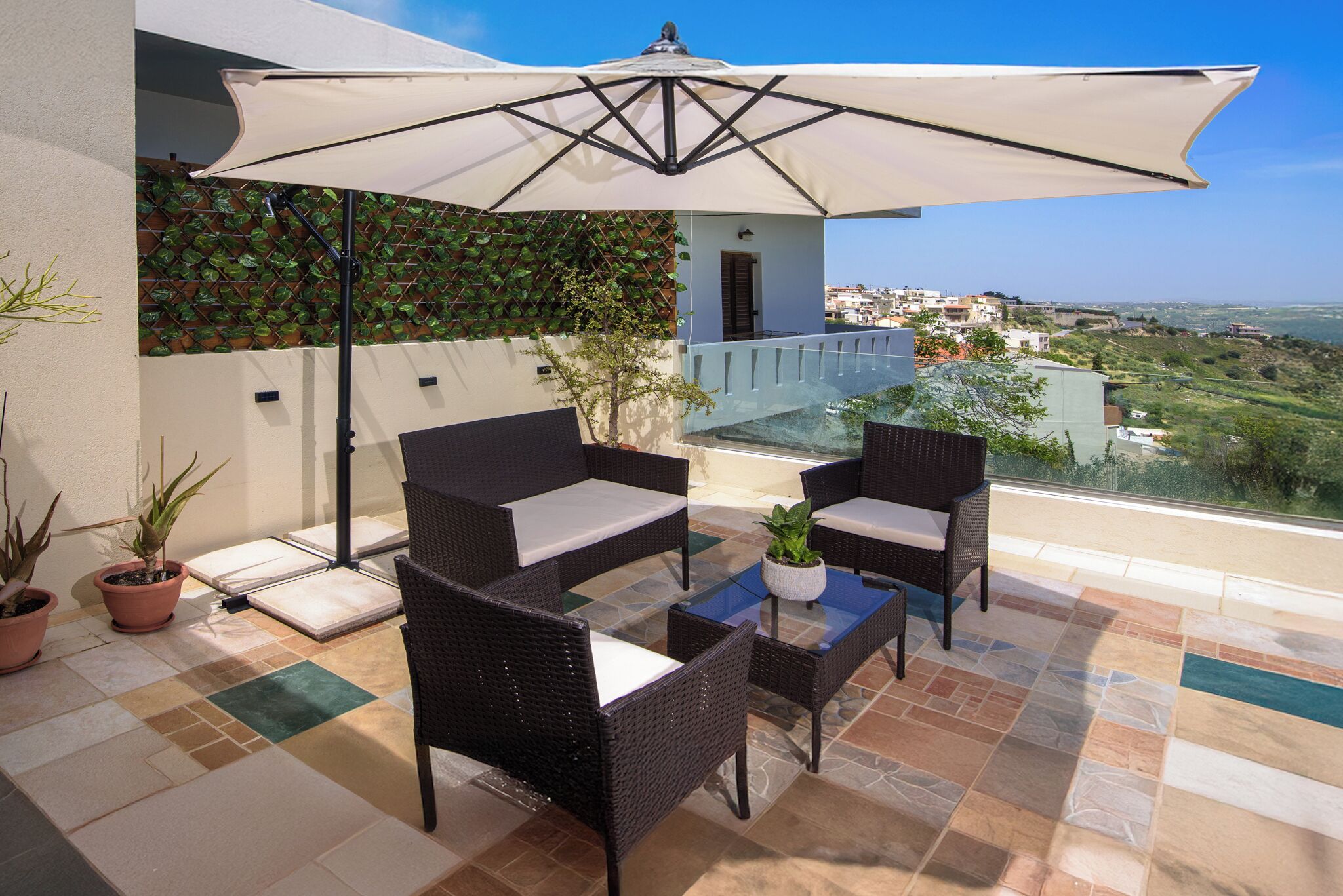 An outdoor seating area with wicker furniture and a large umbrella, overlooking a scenic view.