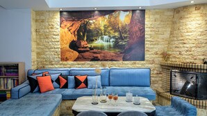 Un salon moderne avec un canapé d’angle, une cheminée et une grande fresque murale sur le thème de la nature.