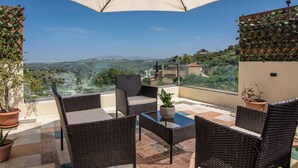 Un balcon agrémenté de meubles en osier, d’une plante en pot et offrant une vue sur le paysage.