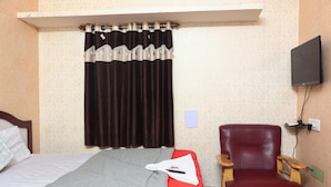 Una habitación de hotel con una cama, un sillón rojo, un televisor de pantalla plana y una ventana con cortinas.