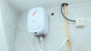 Un baño con pared de mármol blanco, calentador de agua y tubería amarilla.