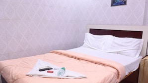 Una cama bien tendida con una manta color melocotón, almohadas blancas y una toalla blanca doblada encima.