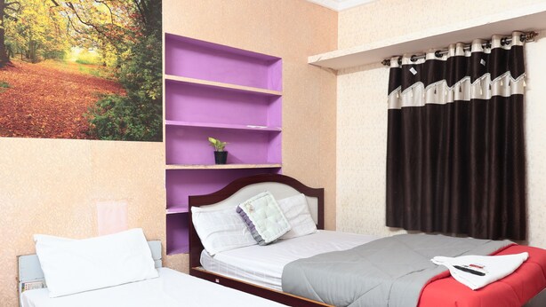 Un dormitorio con dos camas individuales, un estante morado, una cortina negra y un cuadro de un sendero forestal.
