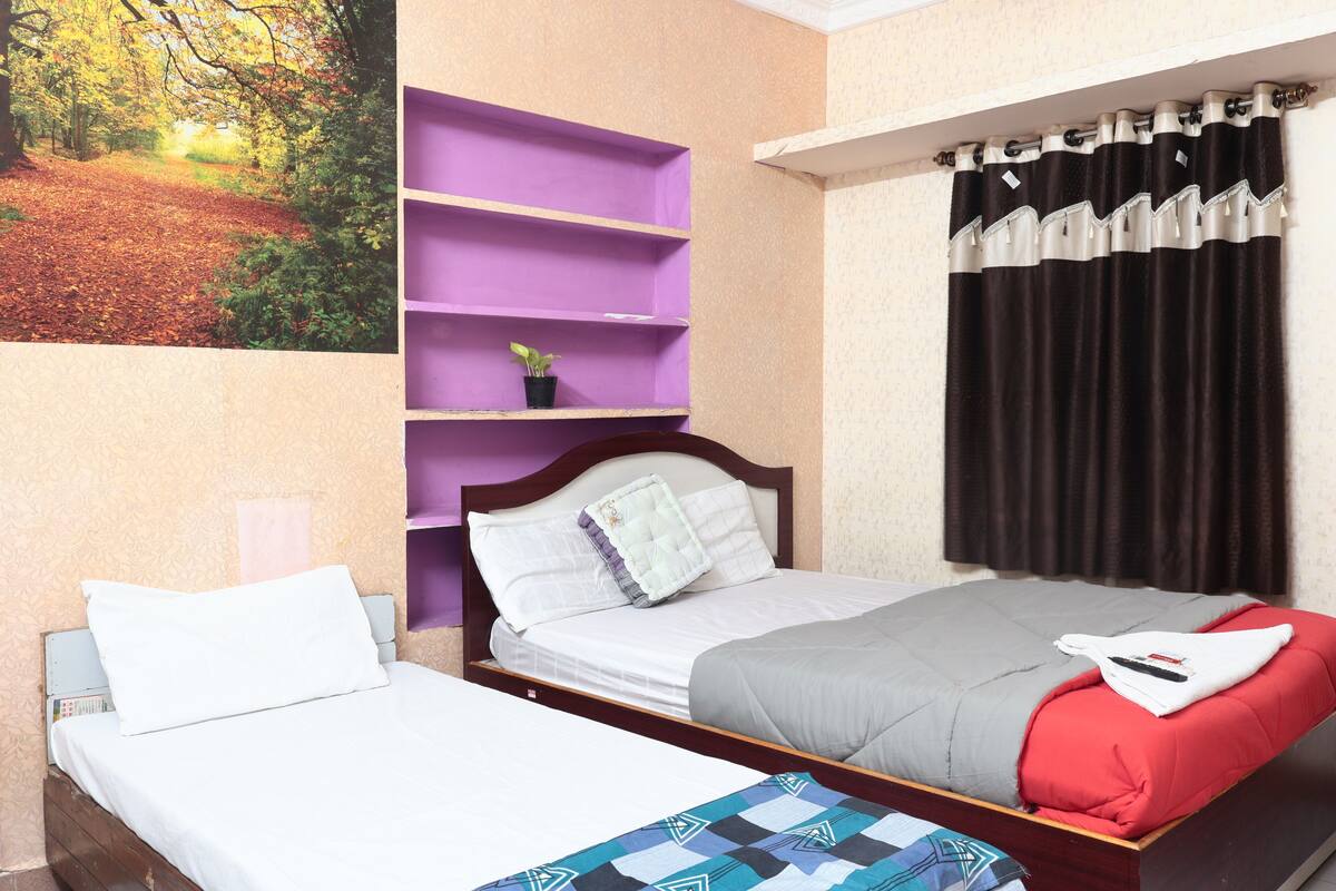 A bedroom with two single beds, a purple shelving unit, a black curtain, and a framed picture of a forest path.