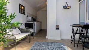 Un espacio habitable pequeño con sofá, una mesa de comedor, una zona de cocina y una planta en maceta.