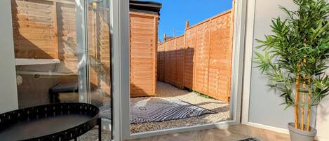 A room with a glass door leading to a backyard, a black outdoor table, a patterned rug, and a bamboo plant.