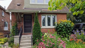 A residential house with a brick facade, a front door, and a small garden with various flowers. - Cozy retreat home in Guelph. Pet-friendly! (Guelph)
