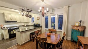 A kitchen with wooden cabinets, a dining table with chairs, a chandelier, and a view of the outside through windows. - Cozy retreat home in Guelph. Pet-friendly! (Guelph)