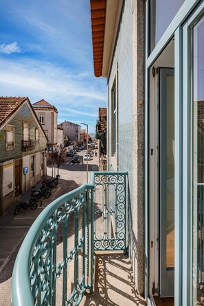 A balcony with a metal railing, a door to a building, and a street view with parked cars and buildings. - Matosinhos Seaside Prime Studio (Matosinhos)