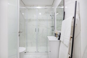A modern bathroom with a glass-enclosed shower, a white toilet, and a sink with a towel hanging on a rack. - Matosinhos Seaside Prime Studio (Matosinhos)