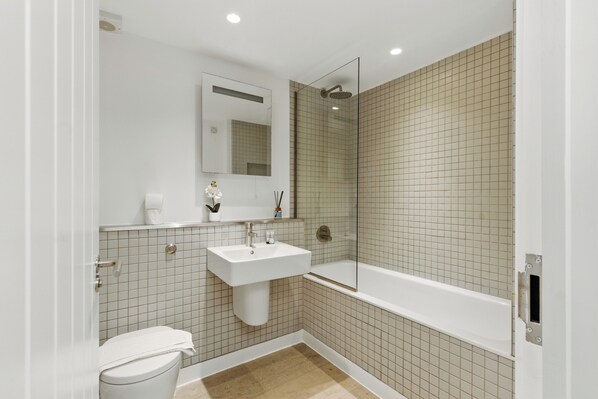 A modern bathroom with a toilet, sink, and glass-enclosed shower.