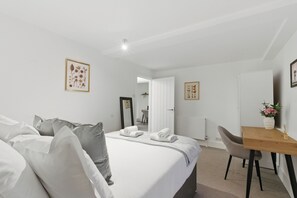 Habitación de hotel con cama, escritorio y silla. Hay toallas sobre la cama y un florero con flores en el escritorio.