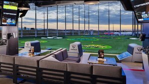 A golf simulation room with a large screen displaying a golf course, multiple screens, and a Topgolf logo.