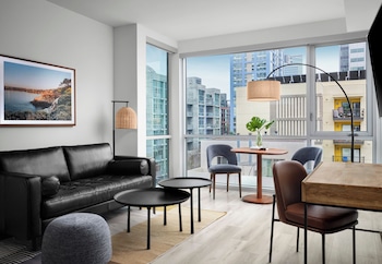 A modern interior with a long wooden table, blue bar stools, a sofa, and large windows offering a view of the street. at The Margot Hotel San Diego Gaslamp Quarter, Outset by Hilton