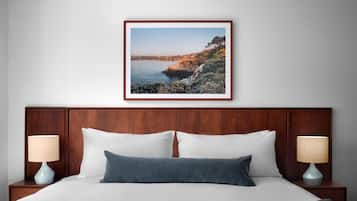 Un letto rifatto con cura, coperto da biancheria bianca e azzurra, due abat-jour e un quadro con un paesaggio costiero incorniciato al muro.