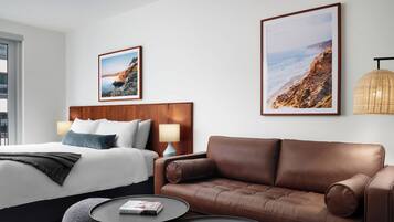 Une chambre d’hôtel avec un lit, un canapé en cuir marron, une table basse ronde et deux tableaux encadrés accrochés au mur.