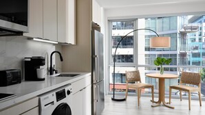 Una cocina moderna con lavadora integrada, cafetera y un amplio ventanal con vistas a edificios.