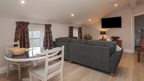 A modern living room with a grey sofa, a dining table with chairs, and a flat-screen TV mounted on the wall. - The Hayloft (Richmond)