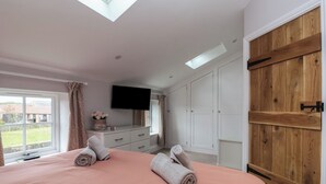A bedroom with a large bed, a TV mounted on the wall, and a wooden wardrobe. - The Hayloft (Richmond)