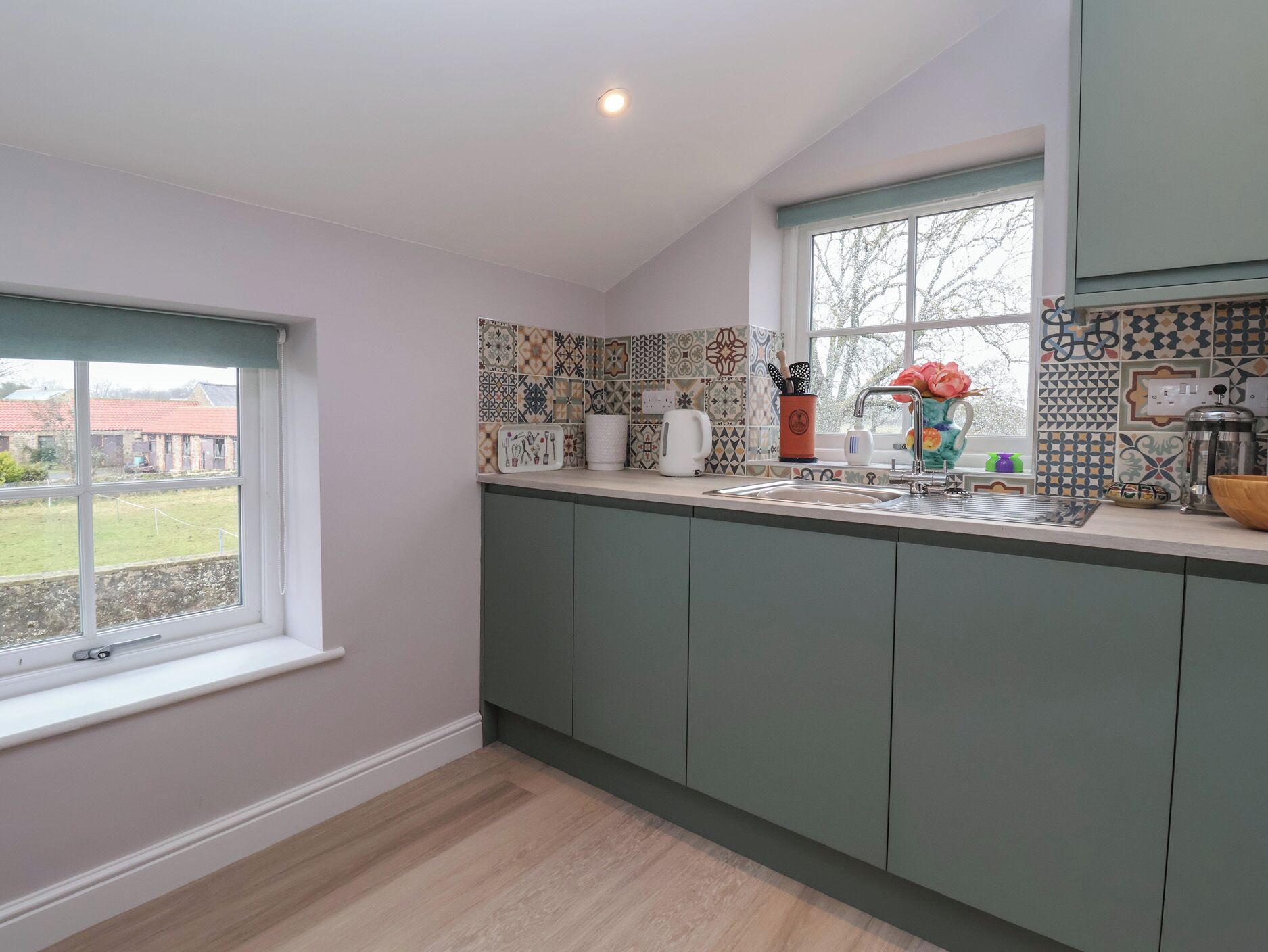 Una cocina moderna con armarios verdes, un ventanal grande y azulejos decorativos en la pared.